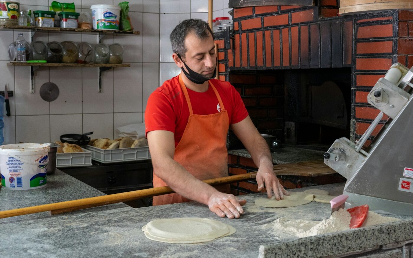 Pizza maker shaping dough beside a wood-fired oven