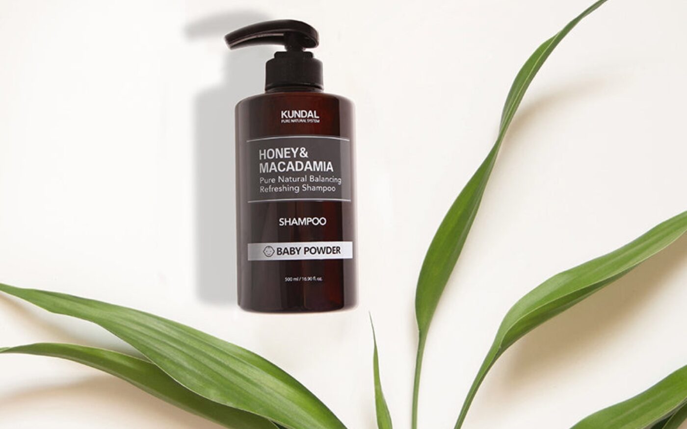 KUNDAL Honey and Macadamia shampoo bottle arranged with green leaves